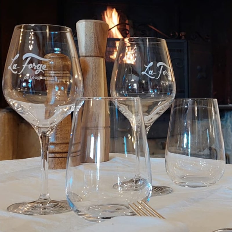 Table avec verres La Forge de Léognan, moulin à poivre, et cheminée allumée en arrière-plan. Ambiance chaleureuse.