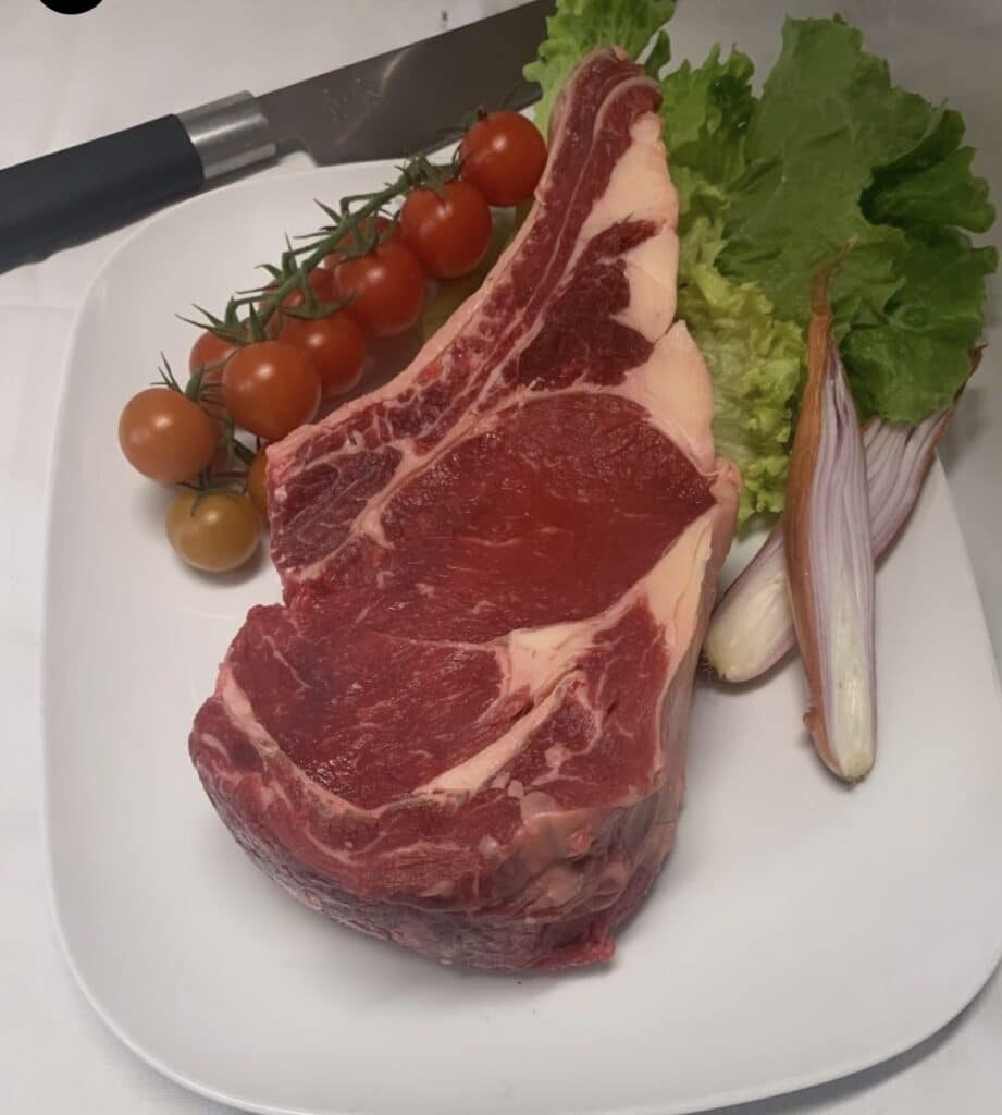 Côte de boeuf crue, tomates cerises en grappe, salade et échalotes sur une assiette avec un couteau de cuisine.