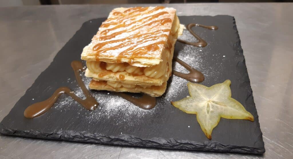 Mille-feuille croustillant au caramel et crème pâtissière sur ardoise noire avec une tranche de carambole.