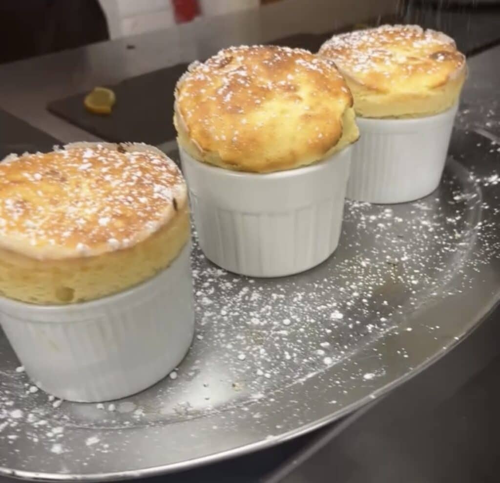 Trois soufflés dorés dans des ramequins blancs sur un plateau d'argent saupoudré de sucre glace.